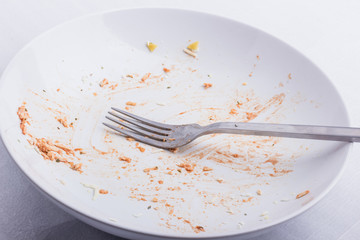An empty, used white plate, with remains of fusilli, covered with tomato sauce and parmesan, with a fork in it