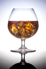 Bicchiere di cristallo a ballon con liquore e cubetti di ghiaccio isolato su sfondo bianco