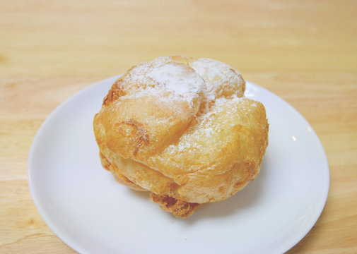 Whole homemade Japanese choux cream puff with icing on a small white plate on a wood table