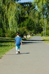Lone small child in sporty street clothing and black hat walks away from camera in a park
