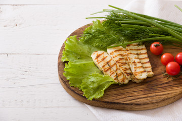 Grilled slices of homemade halloumi cheese with green salad, fresh herbs and organic tomatoes. Fried halloumi cheese with grill marks on white wooden background, top view