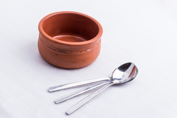 A brown bowl made out of clay and three little spoons