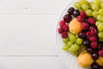 Top view on assortment of juicy fruits on white plate and white table background. Organic raspberries, apricots, melon, cherries - summer dessert or snack. healthy eating concept.