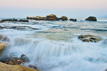 Obraz premium At sunset, waves come in over the rocks in northern Taiwan right next to Yehliu Geopark.