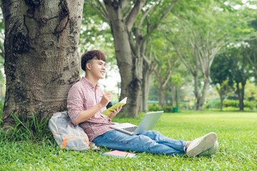 Smiling casual student sitting on grass looking away on campus at college