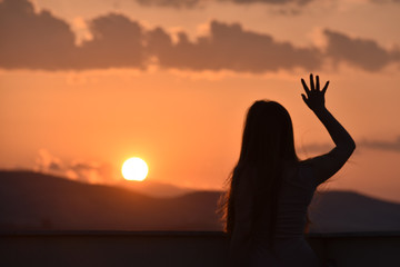 Sunset and silhouette of a girl with long hair looking toward The Sun