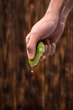 Hand squeeze lime with lime drop on dark wooden background