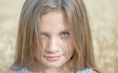 Close-up portrait of adorable little girl with magnetic eyes at a summer day with wheat field background