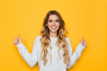 Smiling Young Woman In Pastel Sweater Is Giving Thumbs Up