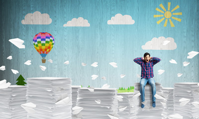 Young man sitting on pile of paper documents.
