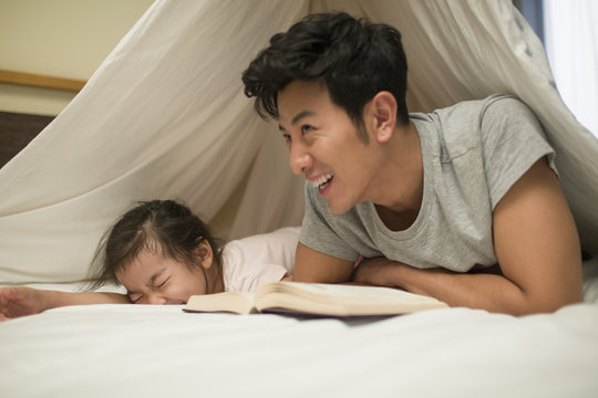 Smiling father and his daughter lying on bed while reading book