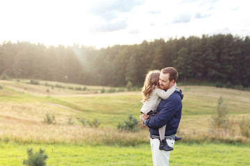 People, relationship, family, happiness concept. Happy father carrying his little daughter, feeling togetherness and love while having walk on green meadow. Cheerful dad and his cute small child