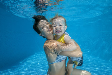 Mom with little daughter under water in pool
