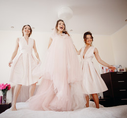 Bride in ivory dress and bridesmaids jump on the bed