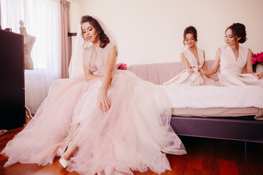 Thoughtful bride and bridesmaids sit on bed in a luxury hotel room