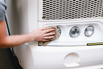 A close-up of a car washer wipes the lights with a sponge truck or bus replacement of candles,...