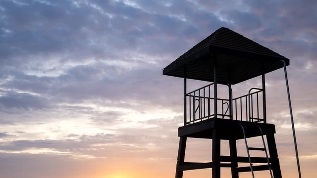 4K Time - lapse Close up life guard tower on the beach with cloud movement and colorful sunset.
