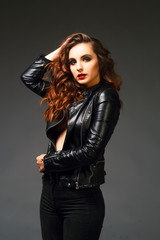 Beautiful young woman posing in black leather jacket over grey background. Fashion concept.