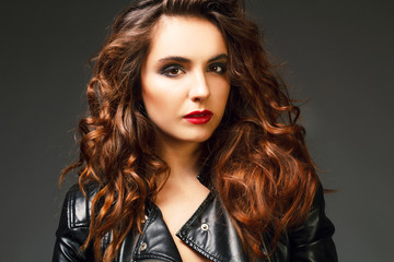 Beautiful young woman posing in black leather jacket over grey background. Fashion concept.