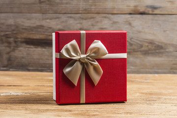 Gift box tied red ribbon with small red hearts printed on it. On old wooden background.