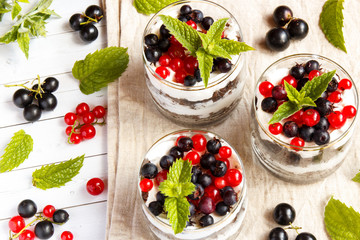 A sweet dessert of sponge cake with cream in a glass with fresh berries on wooden background