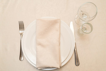 Table with white plate, crystal wineglasses, linen beige napkin and cutlery on tablecloths, top...