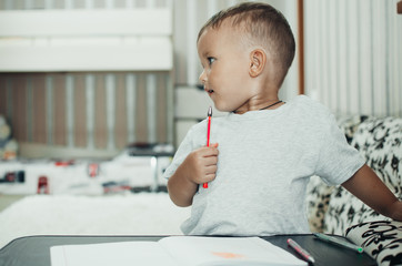 Little baby boy thoughtfully draws or writes pen