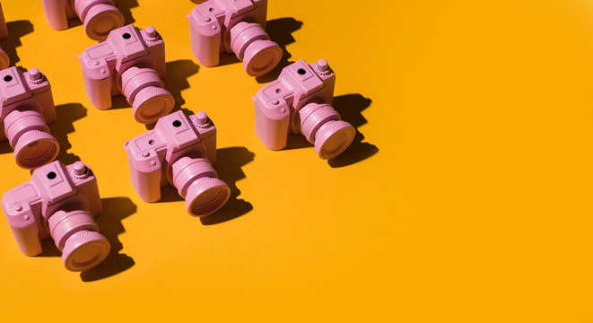 Pink cameras arranged on orange/yellow background.