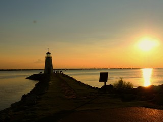 Fototapeta premium A lighthouse silhouetted by a beautiful sunset, with silhouettes of people around