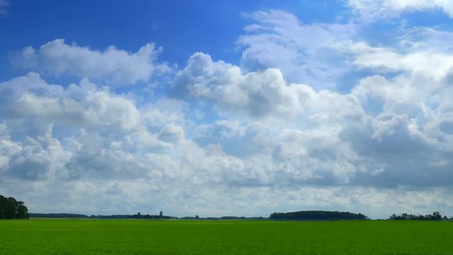 Fluffy clouds drift over green landscape in seamless loop.
