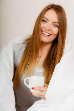 Smiling woman holding cup of drink in bed