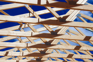 Residential wooden roof trusses against a blue sky in a geometric design.