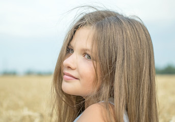 An adorable little girl with beautiful long hair in the wheat field on a warm summer day
