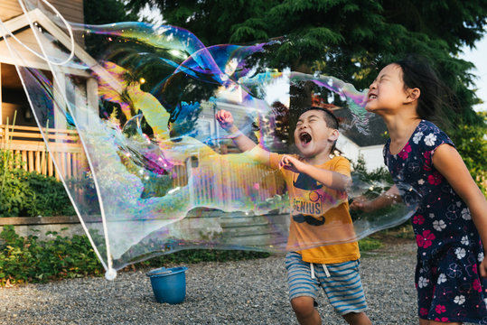 Asian American brother and sister popping a giant bubble outside