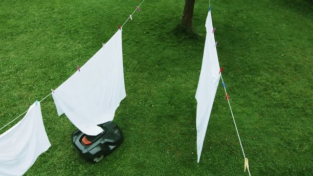 Robot lawn mower mows the lawn in a garden. Laundry on clothes line