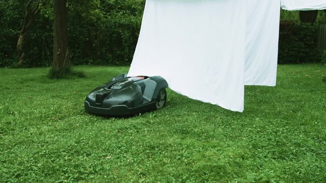 Robot lawn mower mows the lawn in a garden. Laundry on clothes line