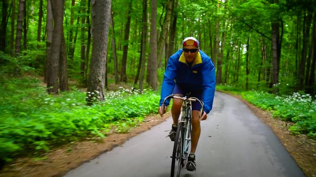 Middle-aged man is riding a road bike along a forest road, slow motion