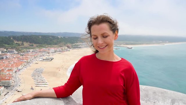 Woman in red dress relaxing on top of a hill above the city of Nazareth, Portugal