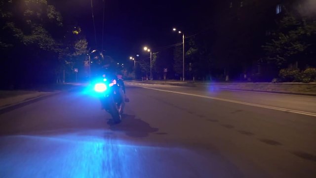 Unrecognizable biker riding a motorcycle on a road surrounded by trees at night