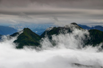 Green ridges of Carnic Alps in clouds with radar station near Monte Terzo and Cimone di Crasulina peaks and in the background Julian Alps, Friuli Venezia Giulia region, Northern Italy, Europe