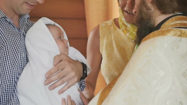 Priest dresses a towel on little baby after a ceremony of baptism in holy water