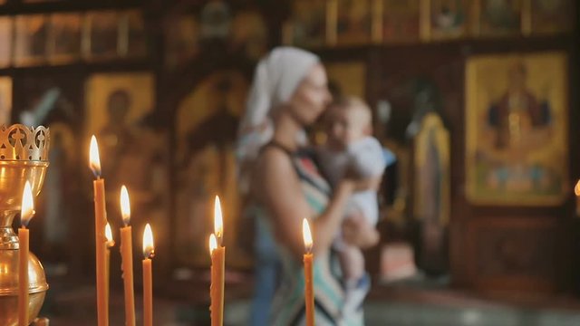 Burning candles in church, mother with baby on blurred background