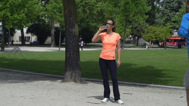 Joggers in city park, man running, woman resting and drinking water super slow motion 240fps
