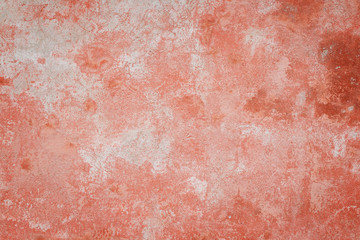 Close-up of a weathered and aged concrete wall, bleached red paint partly peeled off. Texture background with vignette.
