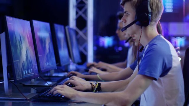 Team of Teenage Gamers Play in MMORPG Video Game on a eSport Tournament. Displays Show Beautiful Game, Players Speak into Headsets Microphones and Actively Play to Win. 