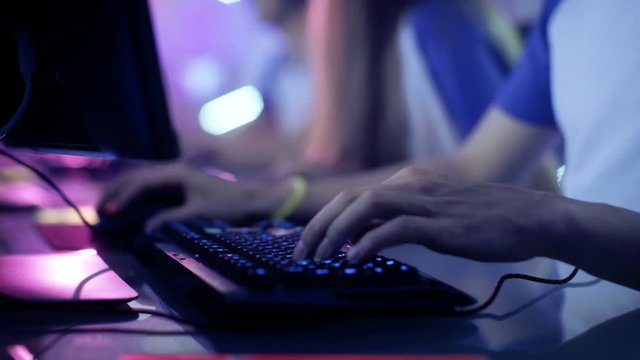 Close-up On Gamer's Hands on a keyboard, Actively Pushing Buttons, Playing MMO Games Online. Background is Lit with Neon Lights. Shot on RED EPIC-W 8K Helium Cinema Camera.