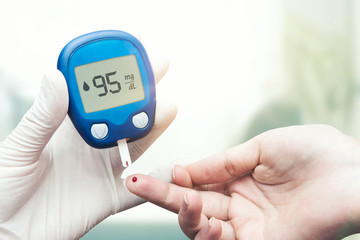 Doctor making blood sugar test. Hands with gloves on medical background