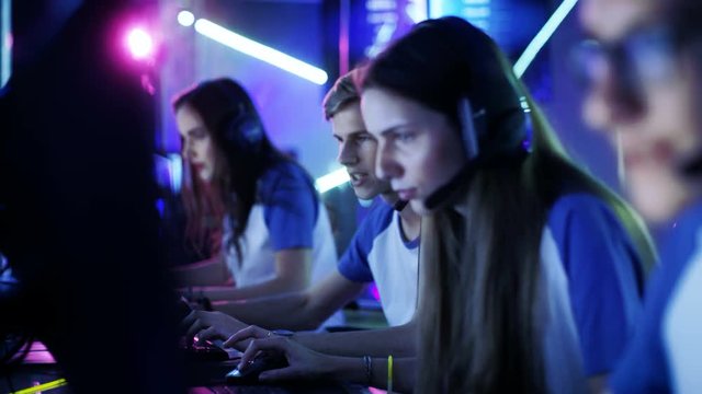Team of Professional eSport Gamers Playing in Competitive Video Games on a Cyber Games Tournament. Girls and Boys Have Headphones On, Arena is Lit with Neon Lights.