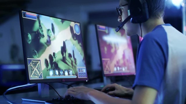 Professional Gamer Plays in MMORPG/ Strategy Video Game on His Computer. He's Participating in Online Cyber Games Tournament, Plays at Home, or in Internet Cafe. He Wears Glasses and Gaming Headsets. 
