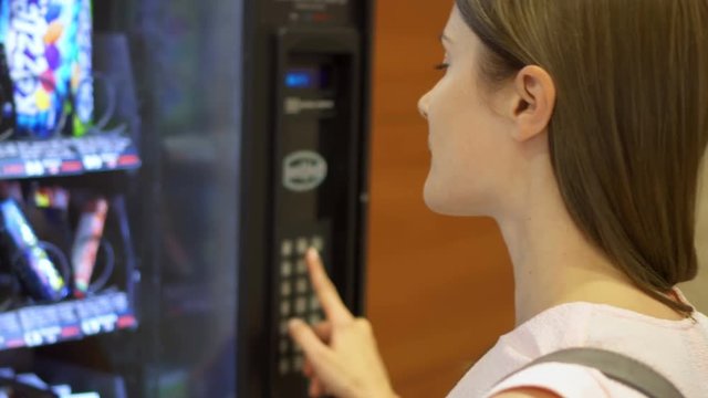 Beautiful hungry woman picking item out of vending machine in mall. Choosing unhealthy snacks being famished